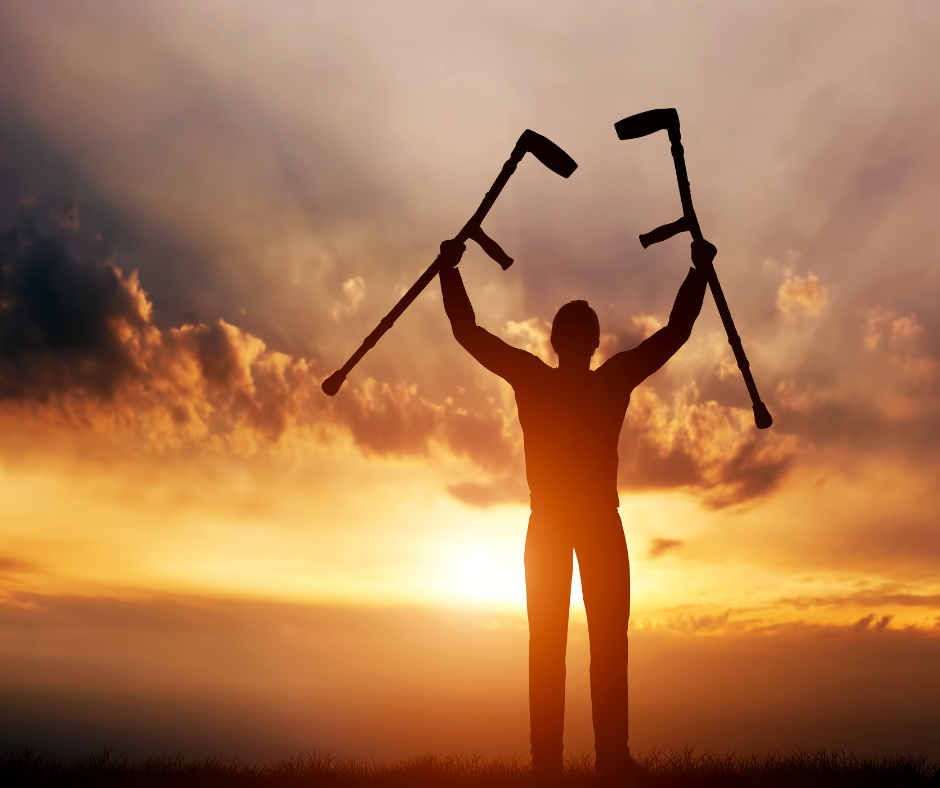 a silhouette of a person holding up crutches as the sun sets