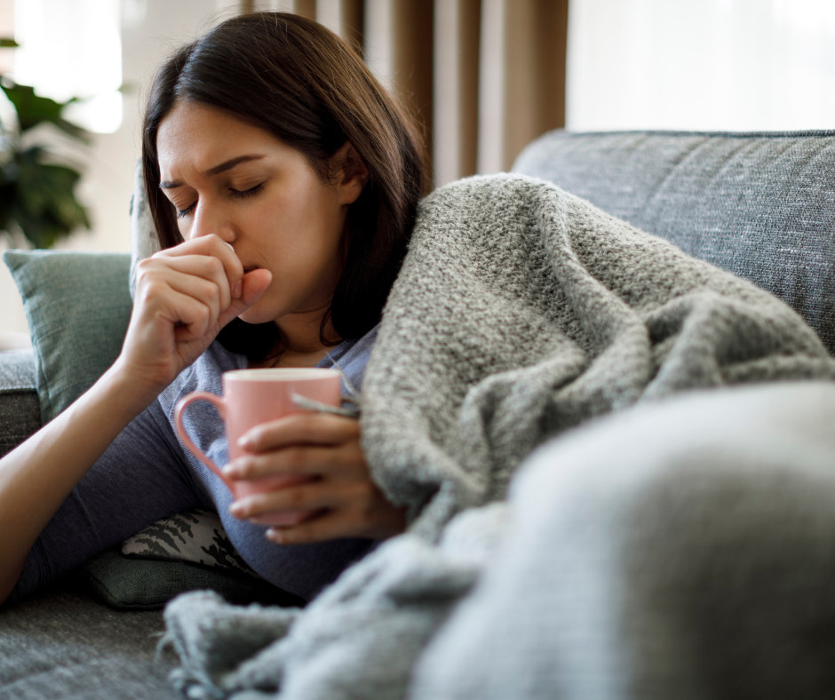 photo of a poorly woman on the sofa coughing and holding a mug.
