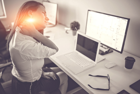 photo of a lady working at a laptop and rubbing her neck in pain